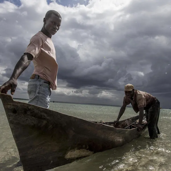 Two men in a canoe at the edge of a waterway with dark clouds in the background.